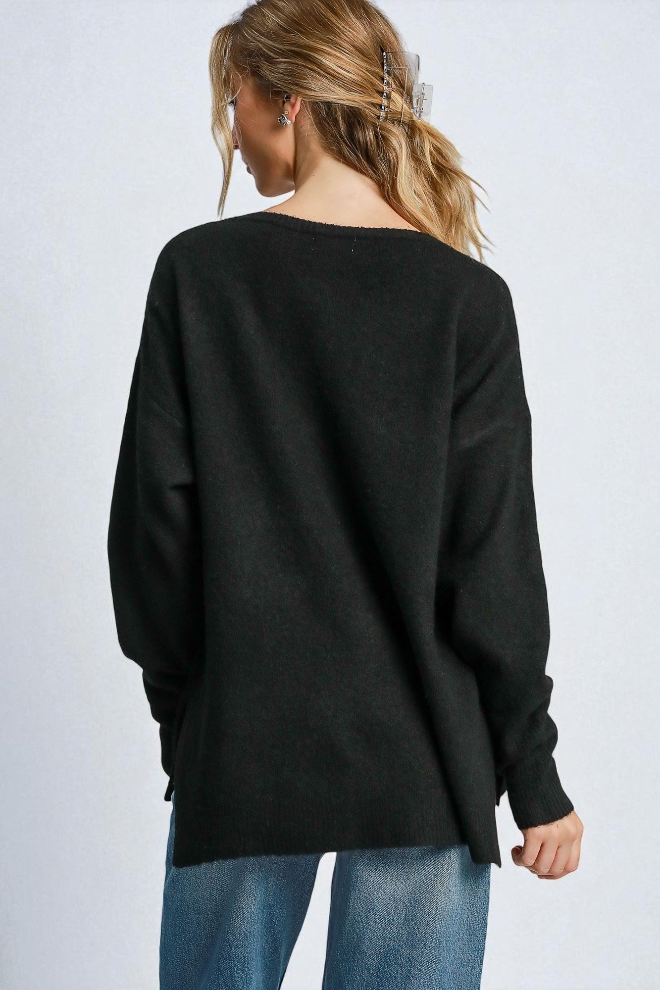 Person wearing a black sweater and blue jeans on a light gray background