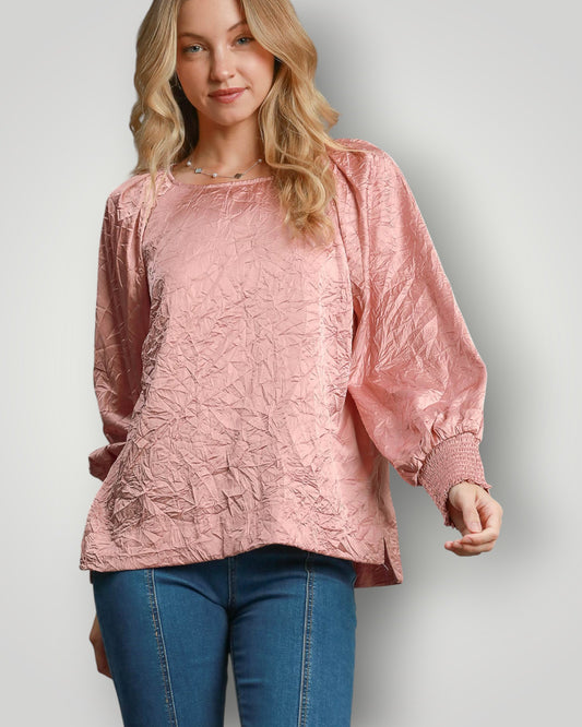 Woman wearing a pink textured top and blue jeans on a plain background