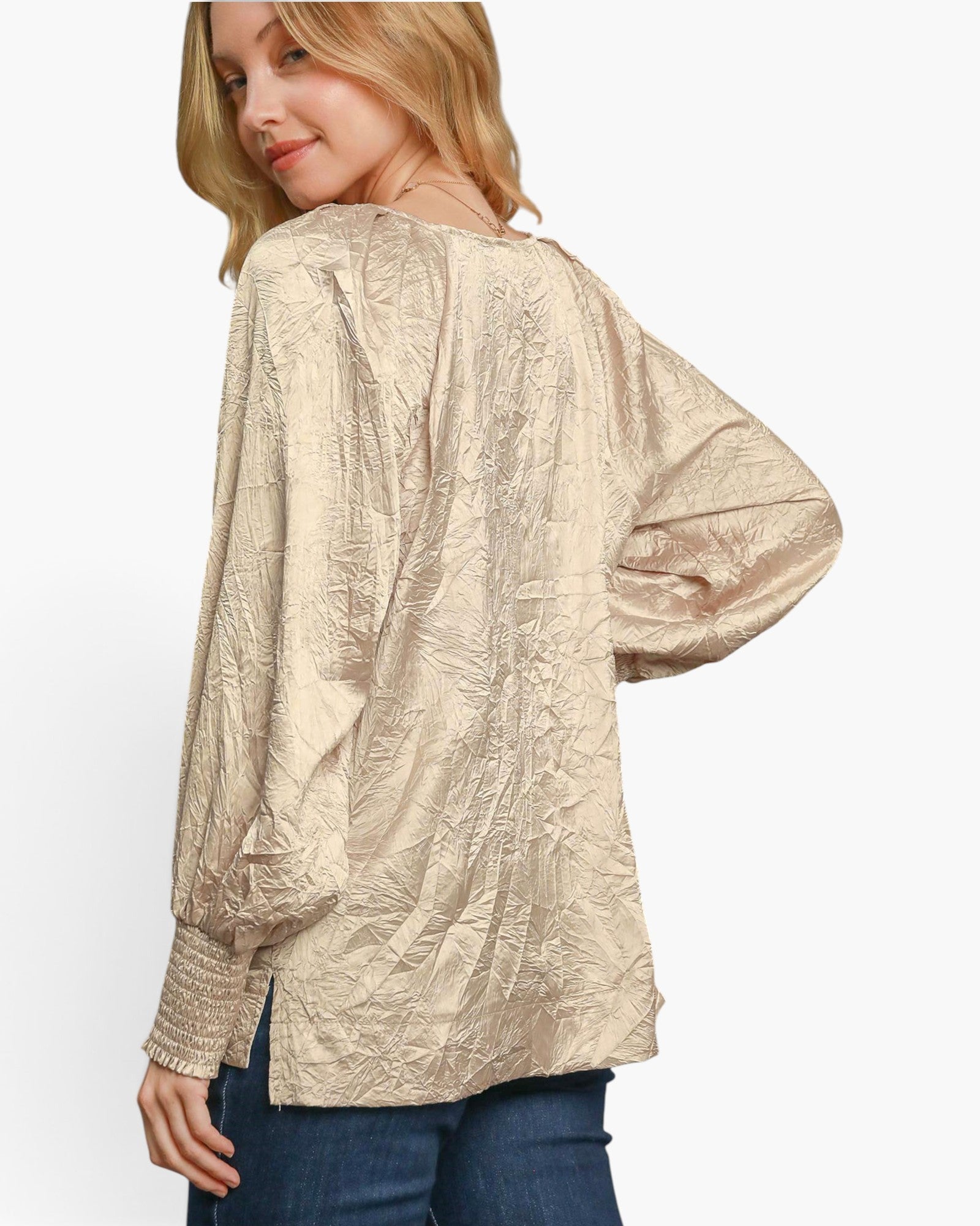 A woman wearing a textured, metallic champagne-beige long-sleeve blouse with a smocked sleeve cuff, shown from a three-quarters back view against a plain white background.