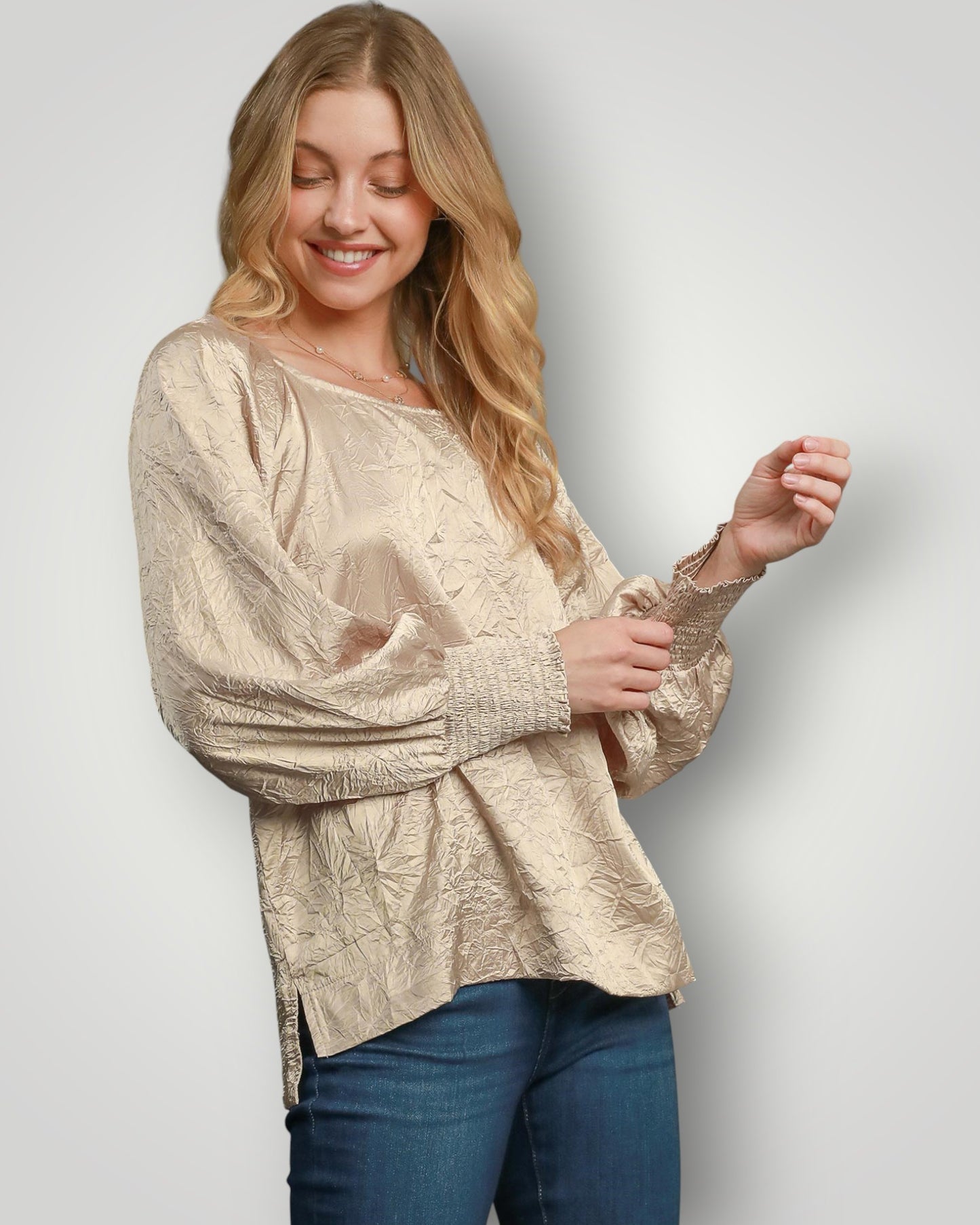 Woman wearing a beige textured blouse and blue jeans against a light gray background