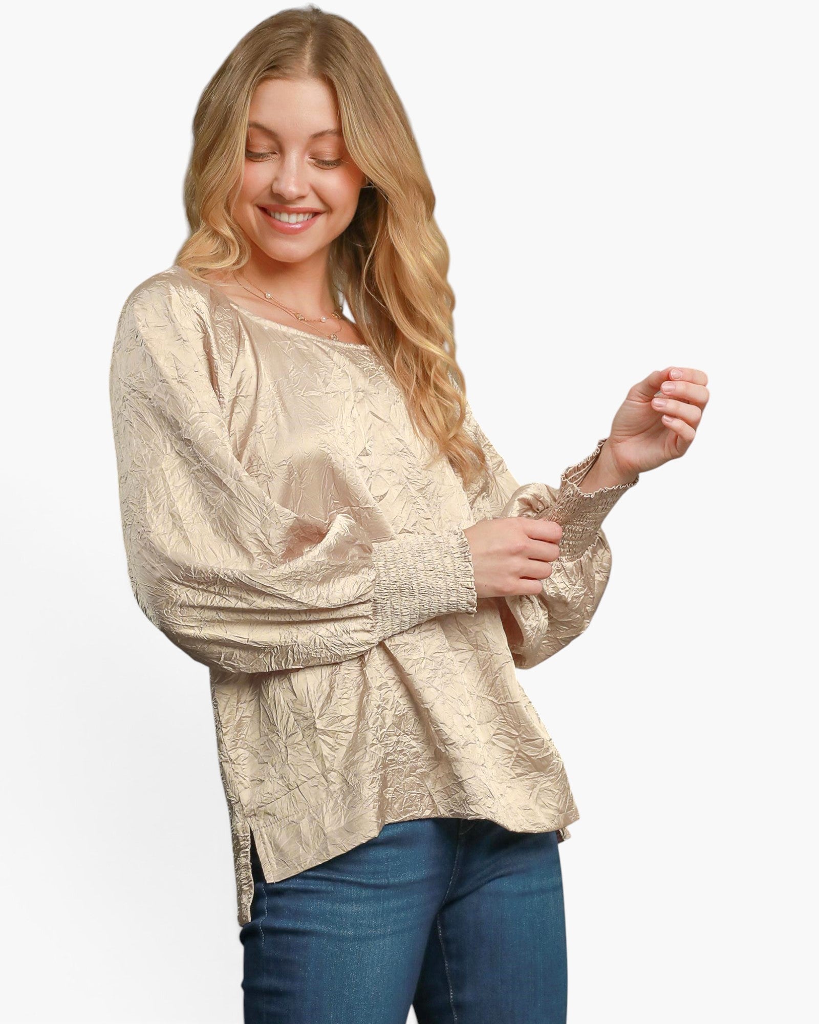 A woman wearing a champagne beige textured long-sleeve top and blue jeans, posing against a solid white background.