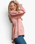 A woman modeling a metallic pink long-sleeve blouse with a crinkled texture and smocked cuffs, paired with blue jeans, against a plain white background.