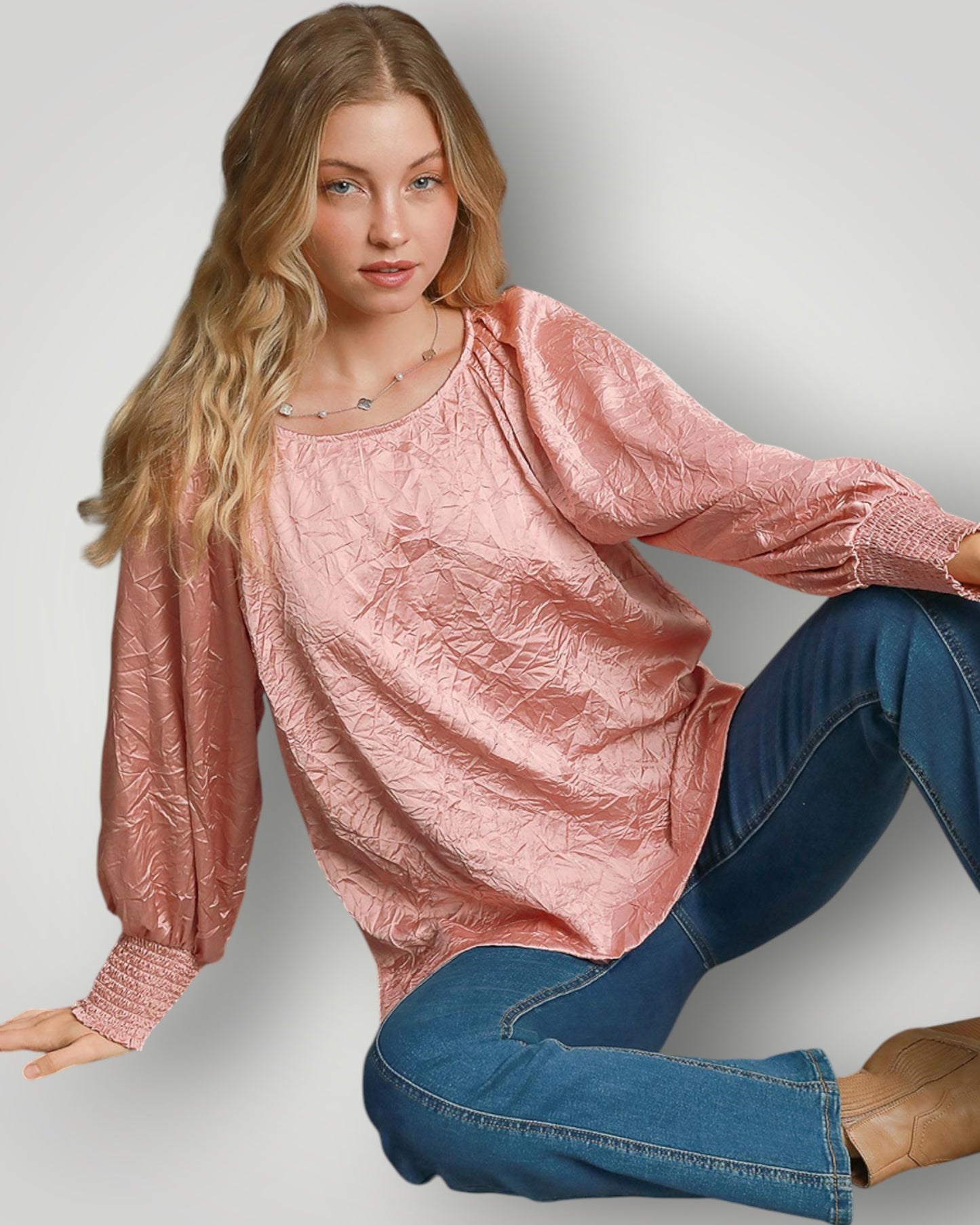Woman wearing a pink textured top and blue jeans on a plain background