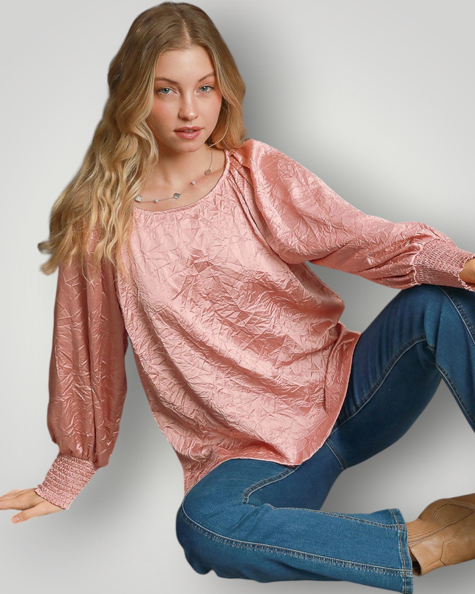 Woman wearing a pink textured top and blue jeans on a plain background