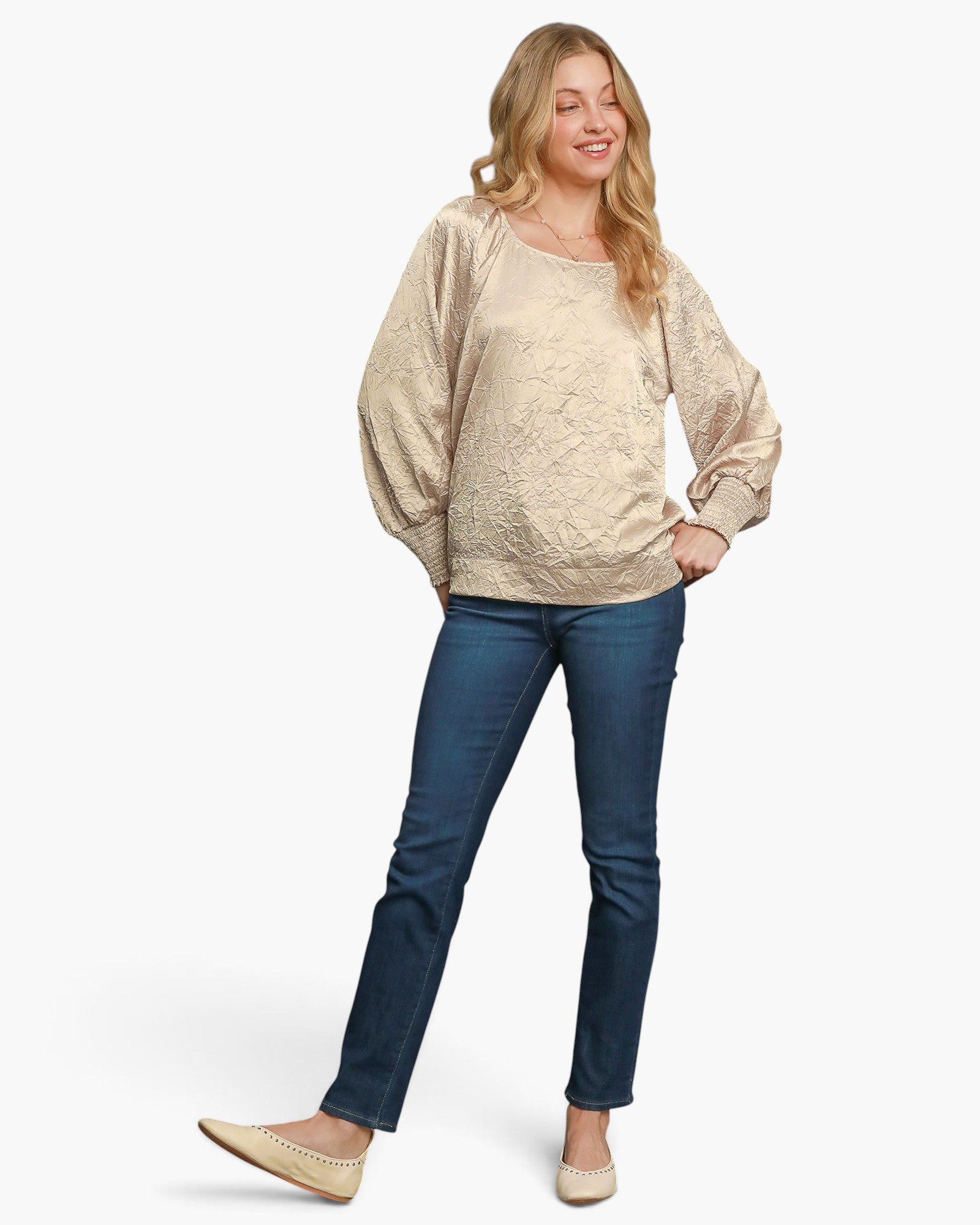 A pregnant woman modeling a champagne beige textured long-sleeve top and dark blue jeans against a plain white background.