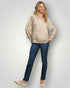 Woman wearing a beige sweater and blue jeans against a white background