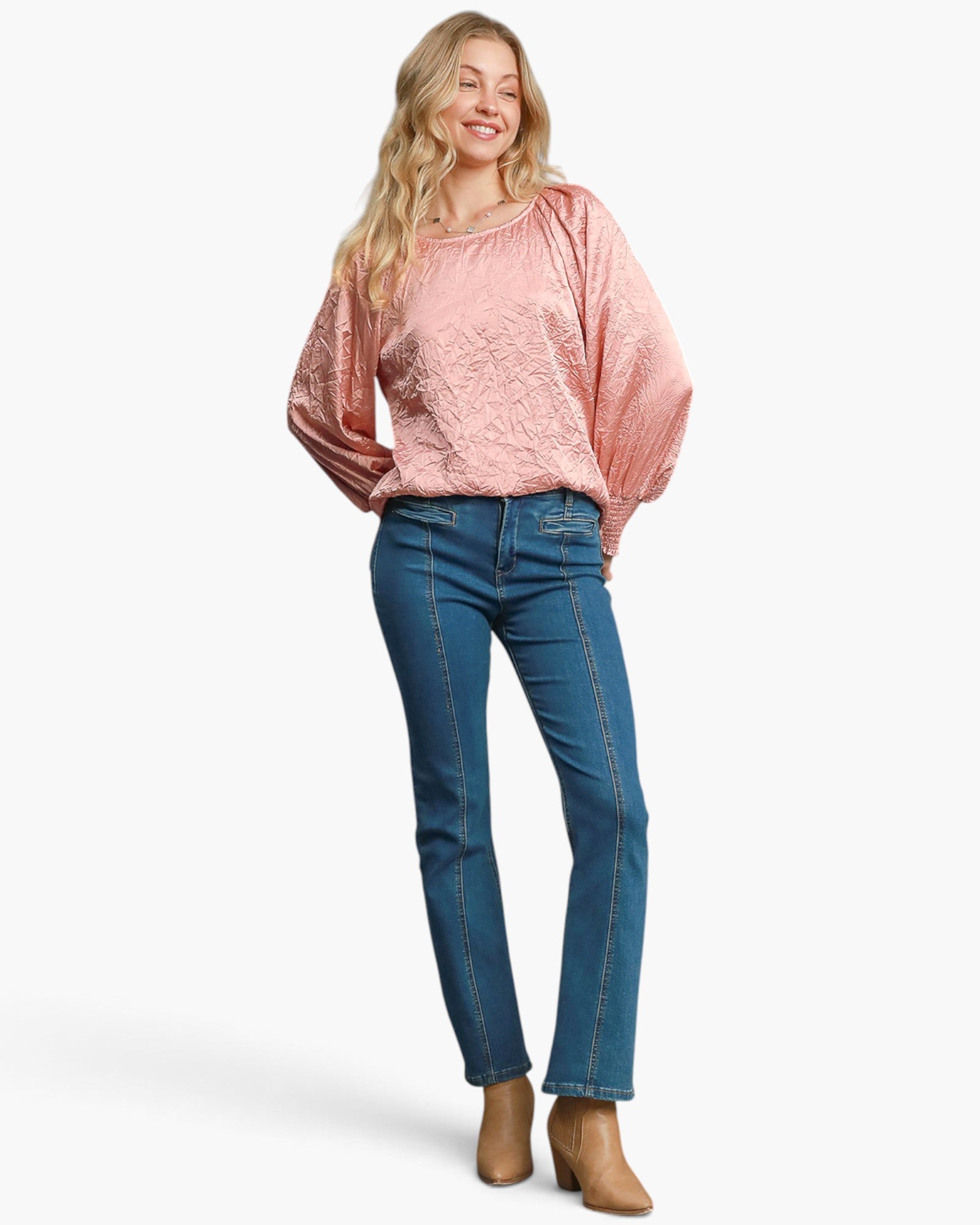 A woman modeling a light pink textured long-sleeve top and blue jeans against a plain white background.
