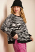 Woman wearing a zebra print sweater and black hat against a beige background