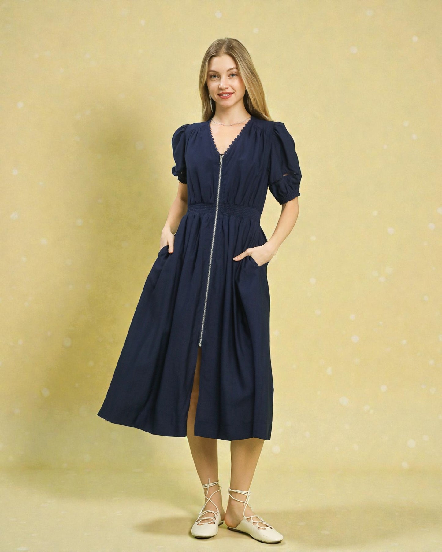 Woman wearing a navy blue dress with puff sleeves on a beige background