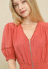 Woman wearing a salmon-colored dress with a zipper detail on a beige background