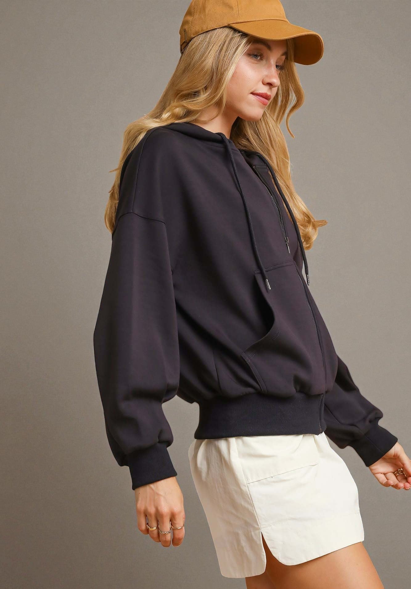 Woman wearing a black hoodie, beige cap, and white shorts on a gray background