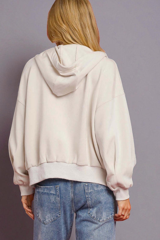 Person wearing a beige hoodie and blue jeans on a gray background