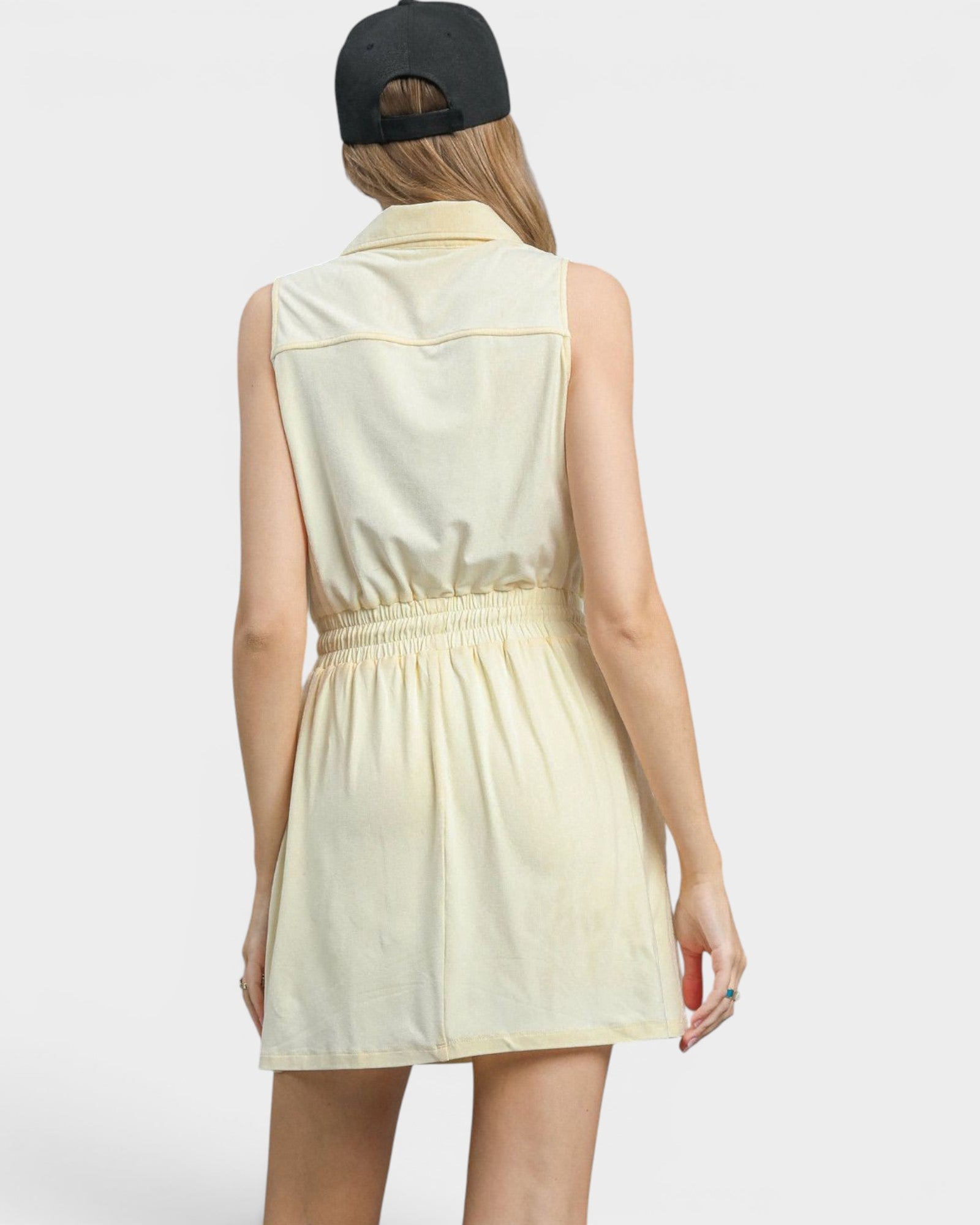 Woman wearing a light yellow sleeveless dress with a black cap on a white background