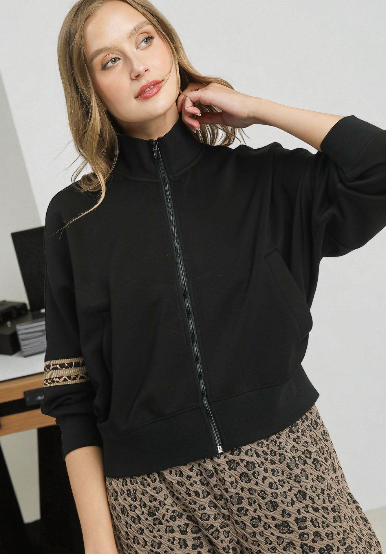Woman wearing a black zip-up sweatshirt with leopard print cuffs in an indoor setting.