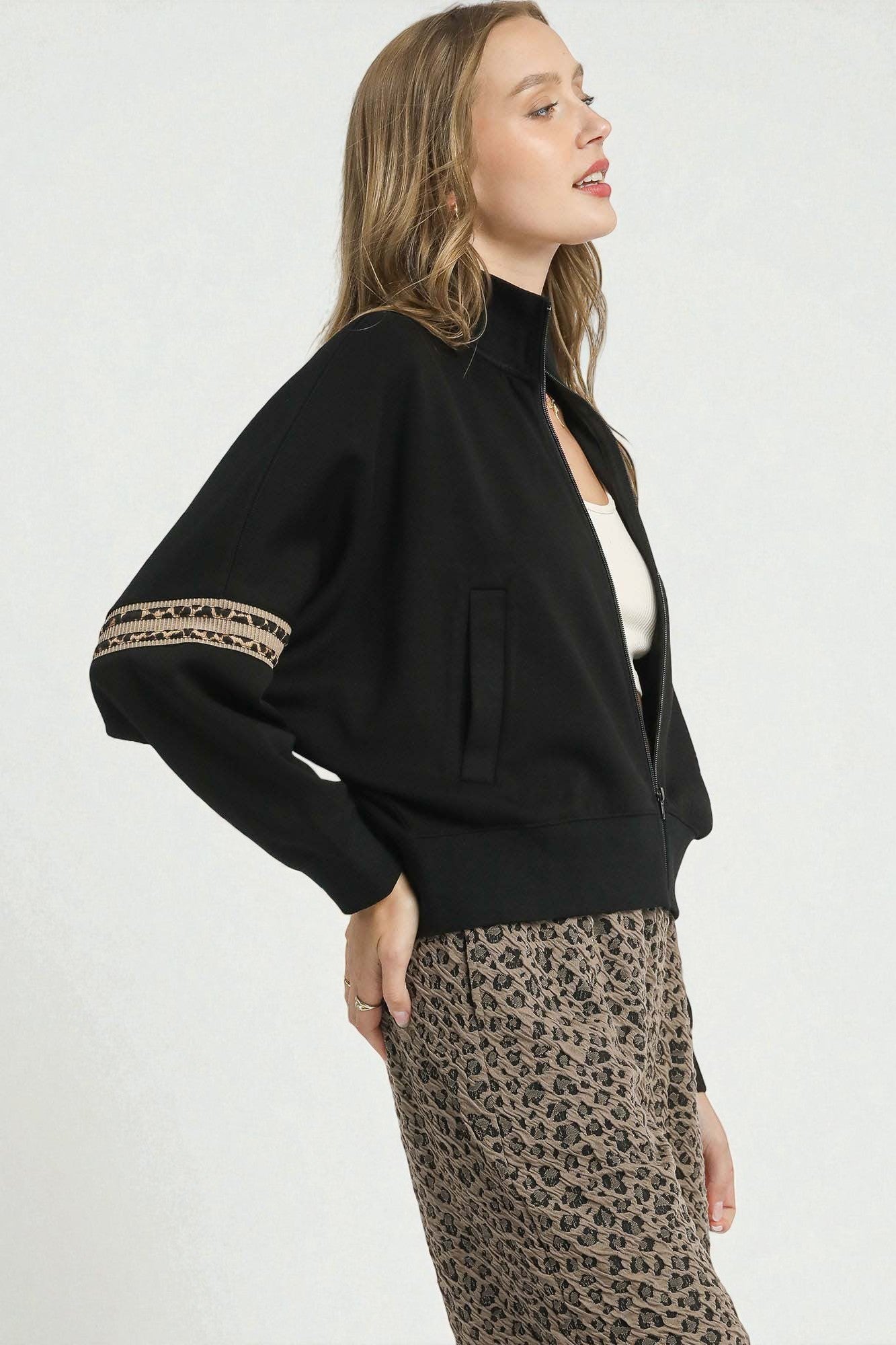 Woman wearing a black jacket with leopard print accents and leopard print pants on a white background