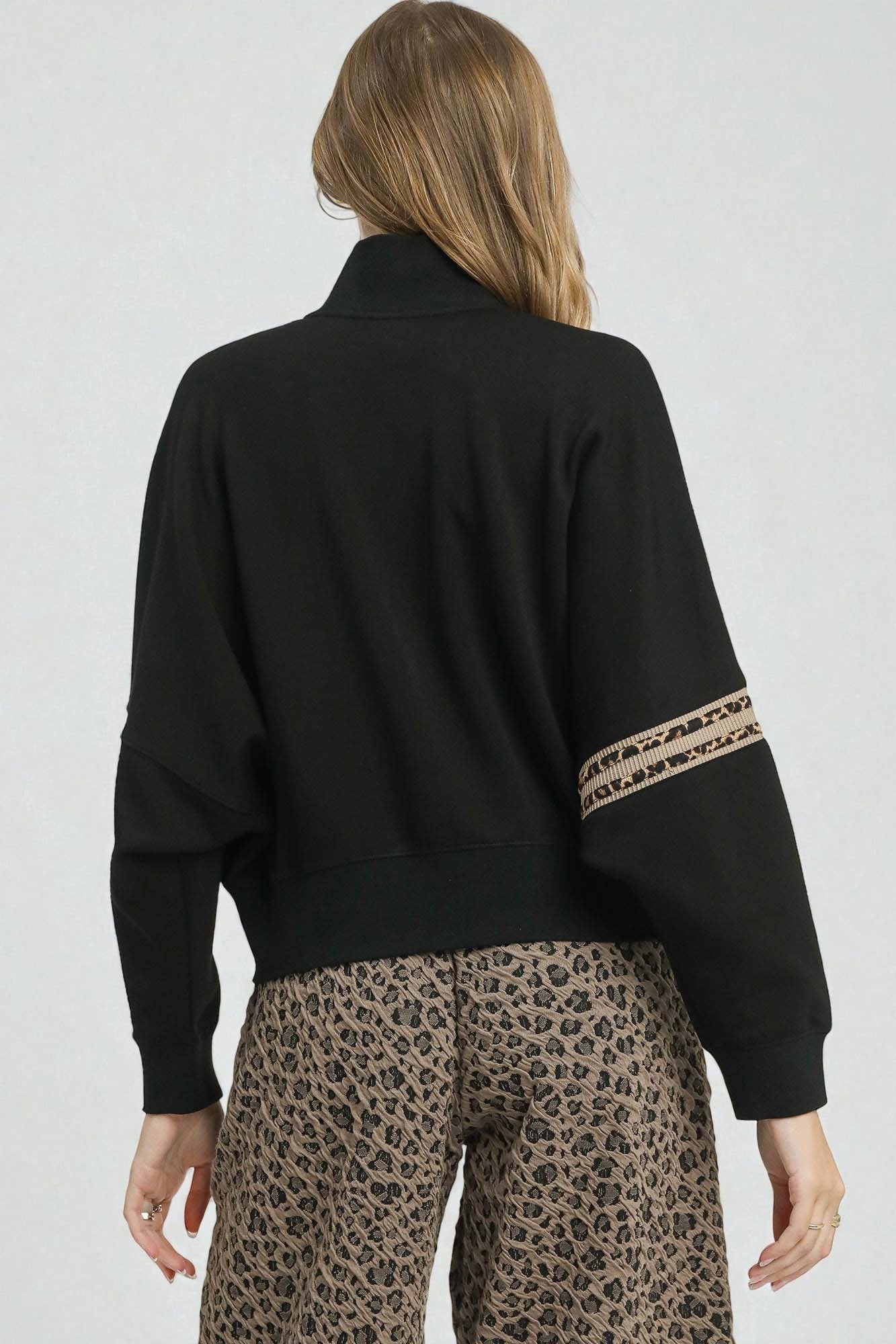 Person wearing a black sweater with leopard print cuffs and a plain background