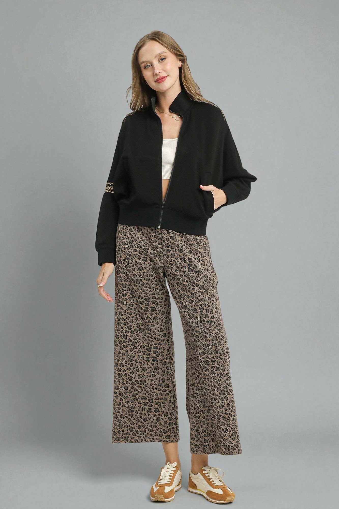 Woman wearing a black jacket, white top, and leopard print pants on a gray background