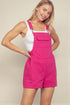 Woman wearing a pink denim overall dress against a plain background