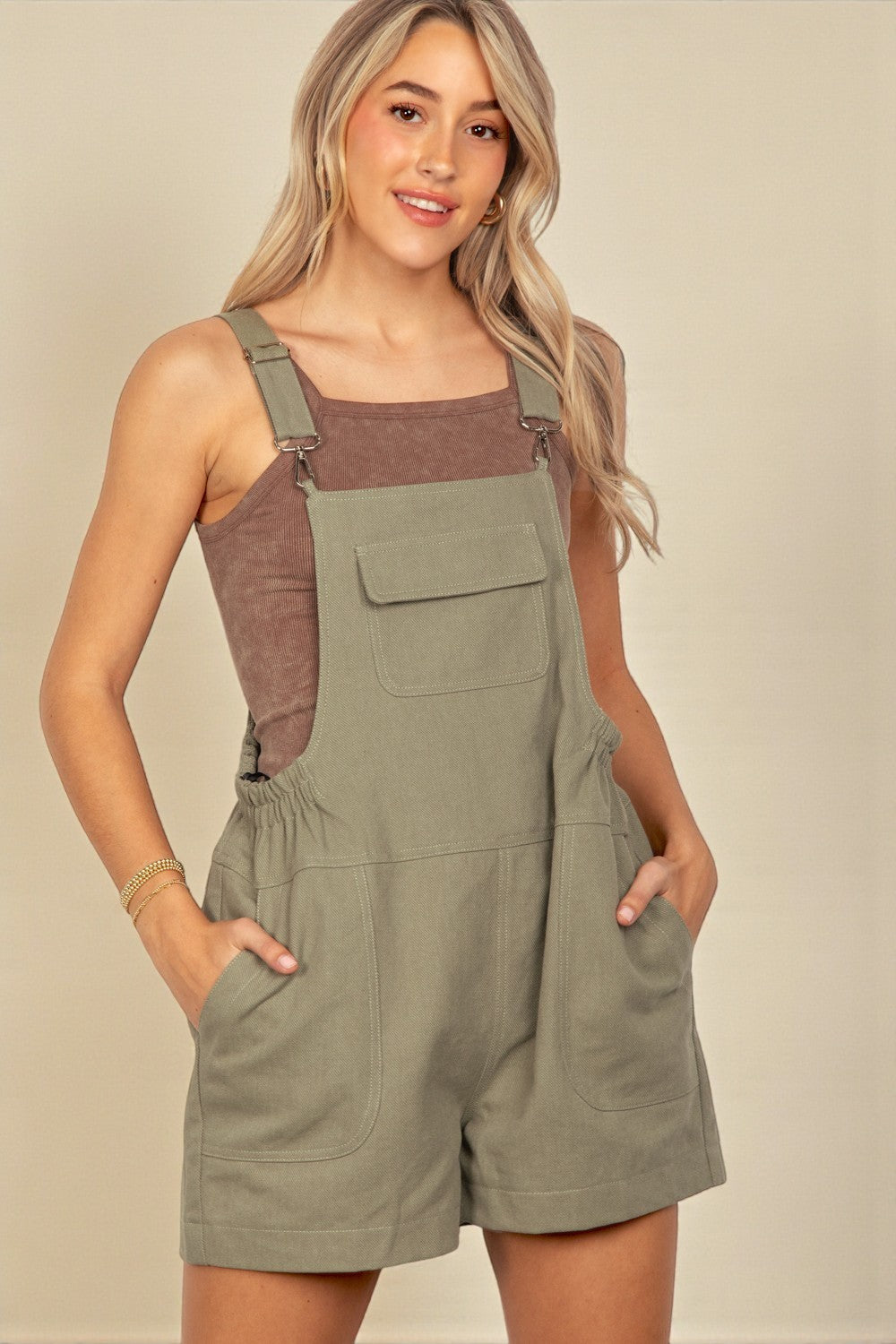 Woman wearing a green overalls with a brown top against a beige background