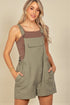 Woman wearing a green overalls with a brown top against a beige background