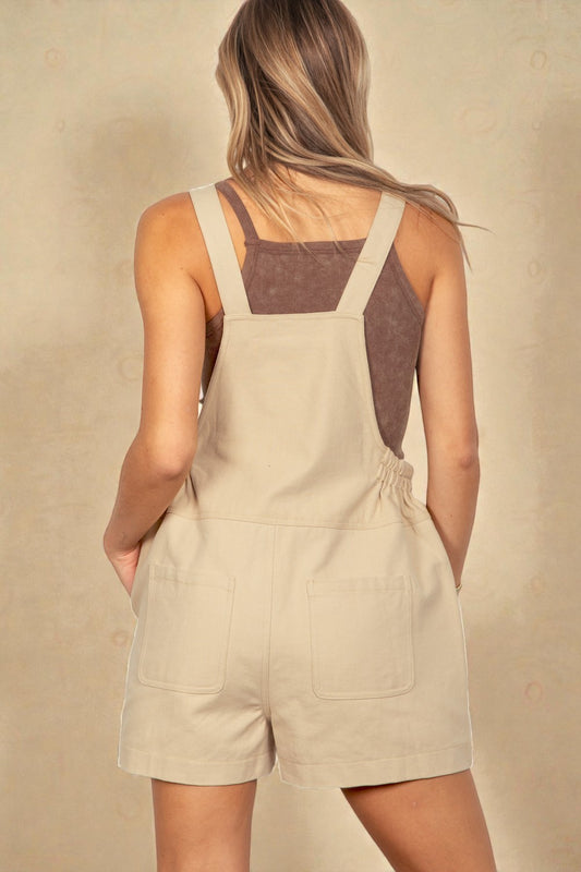 Person wearing beige overalls with a plain background