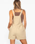 A woman shown from the back wearing a beige short overall jumpsuit over a brown tank top, against a plain white background.
