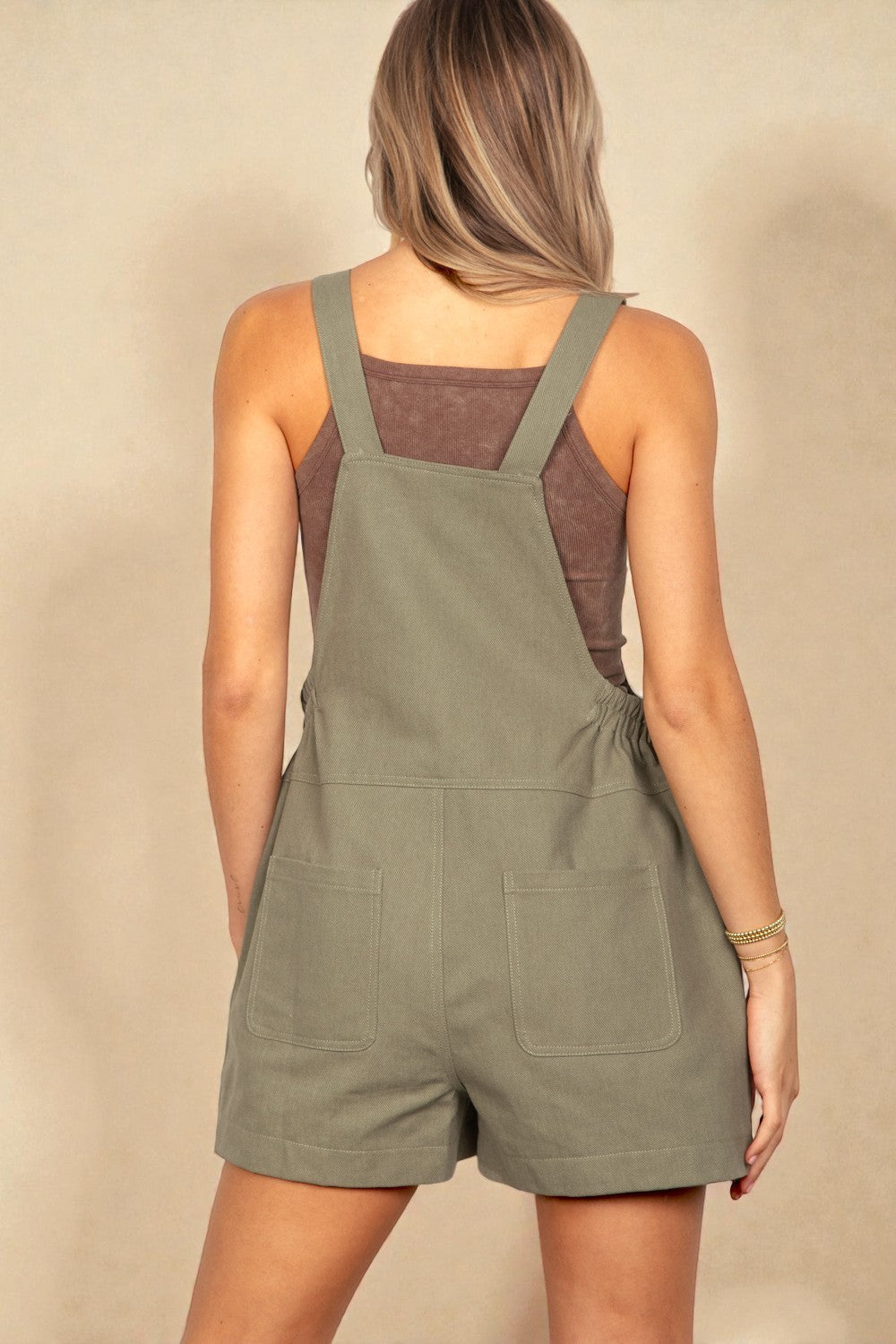 Person wearing a green overall romper against a beige background