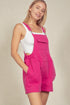 Woman wearing a pink overall dress with a white top against a beige background