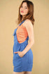 Woman wearing a blue denim dress over an orange top against a beige background