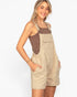 A woman modeling a pair of beige utility bib shorts with a brown textured tank top underneath, set against a plain white studio background.