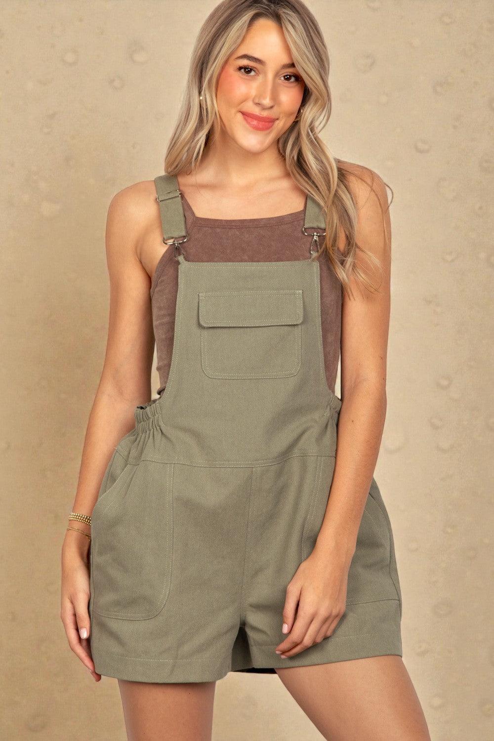 Woman wearing a green overall dress against a beige background