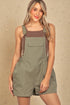 Woman wearing a green overall dress against a beige background
