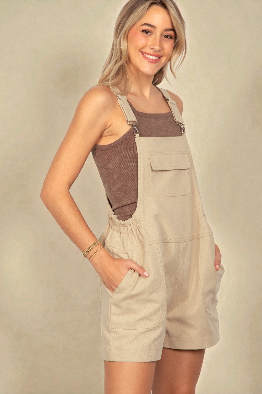 Woman wearing a beige and brown overalls against a plain background