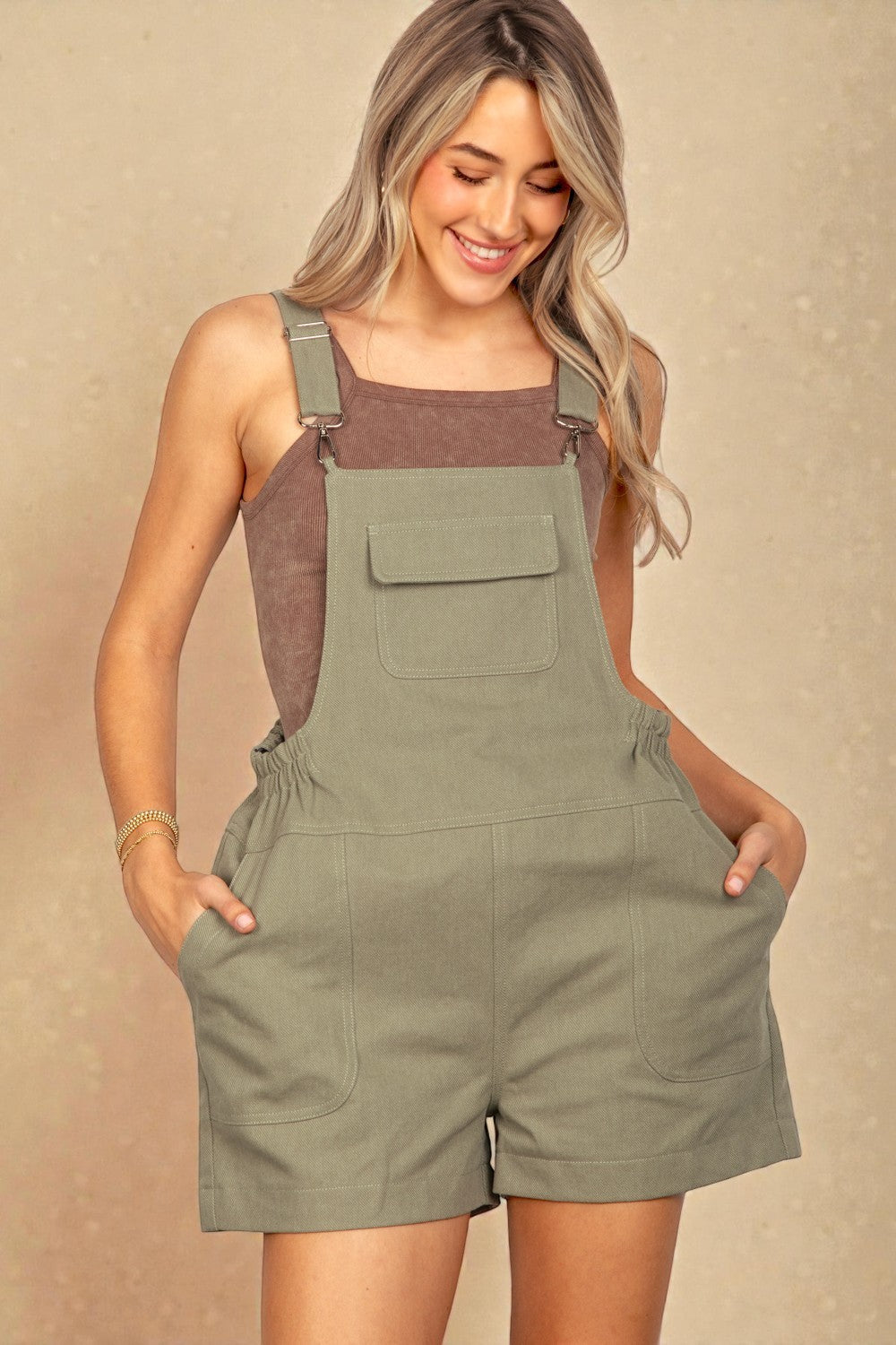 Woman wearing a green overall dress against a beige background