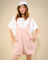Person wearing a white shirt, pink overalls, and a white bucket hat on a beige background