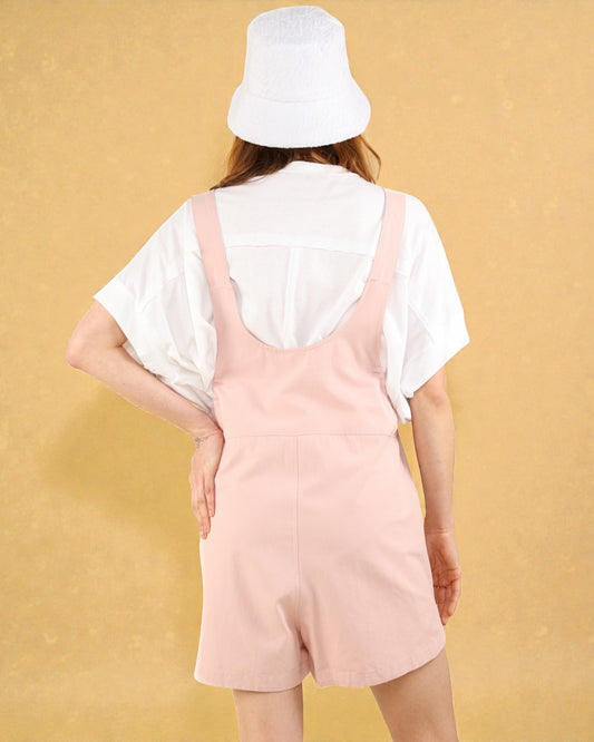 Person wearing a white shirt and pink romper with a white bucket hat against a beige background