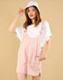 Woman wearing a pink pinafore dress over a white shirt with a beige background