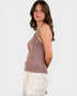 Woman wearing a brown tank top and white pants on a plain background