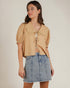 Woman wearing a beige blouse and denim skirt on a plain background