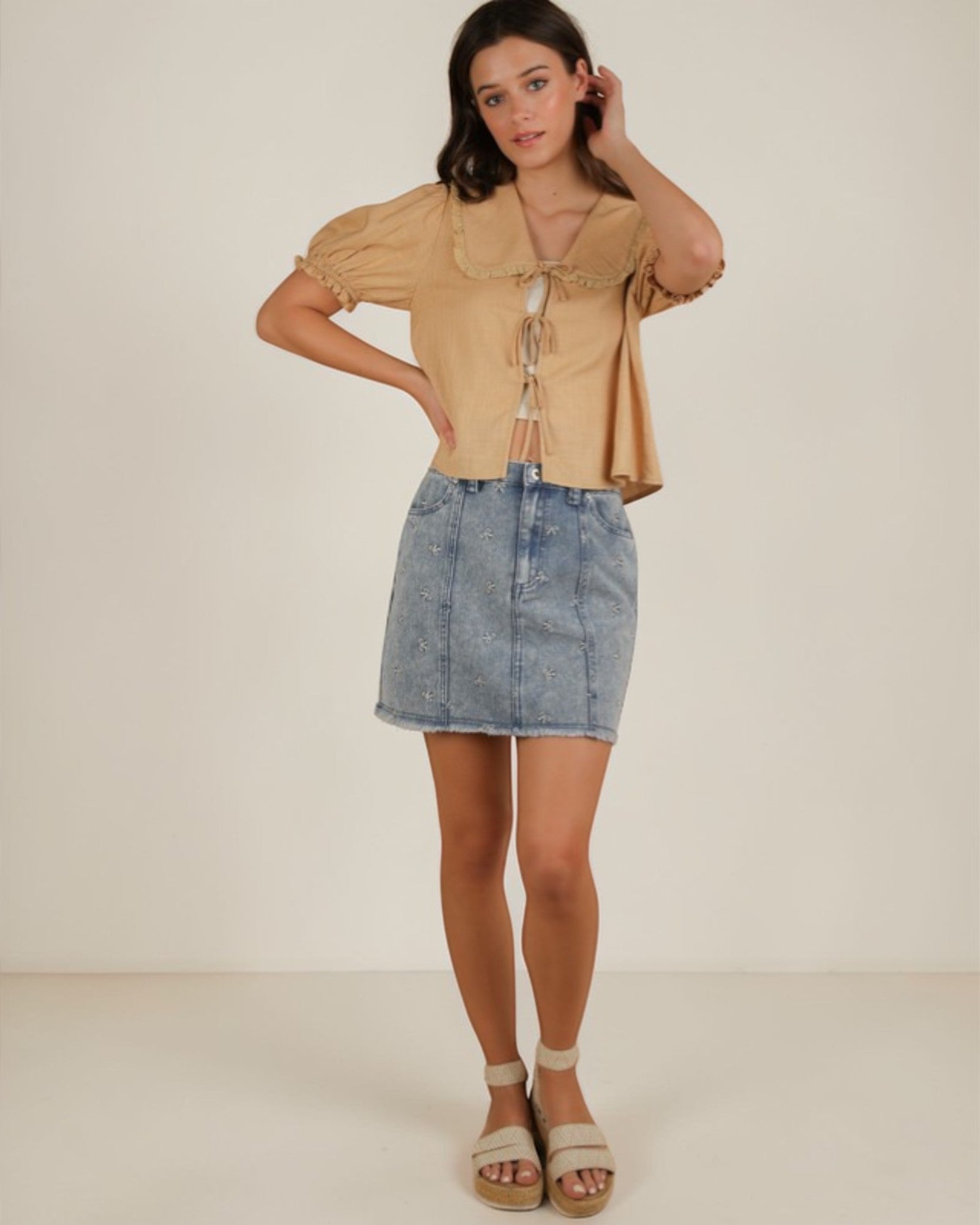 Woman wearing a beige top and denim skirt on a white background
