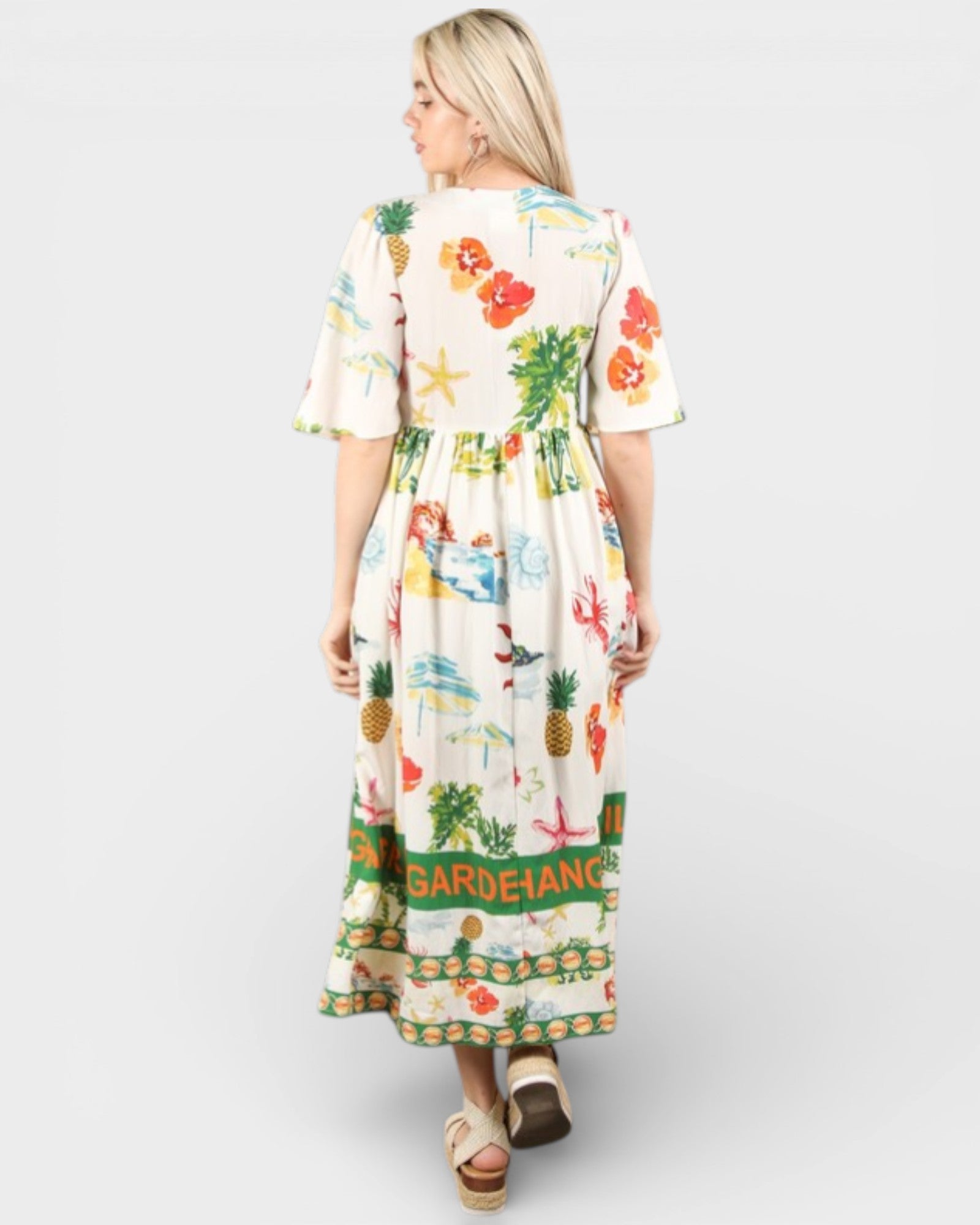 Woman wearing a colorful dress with floral and pineapple patterns on a white background