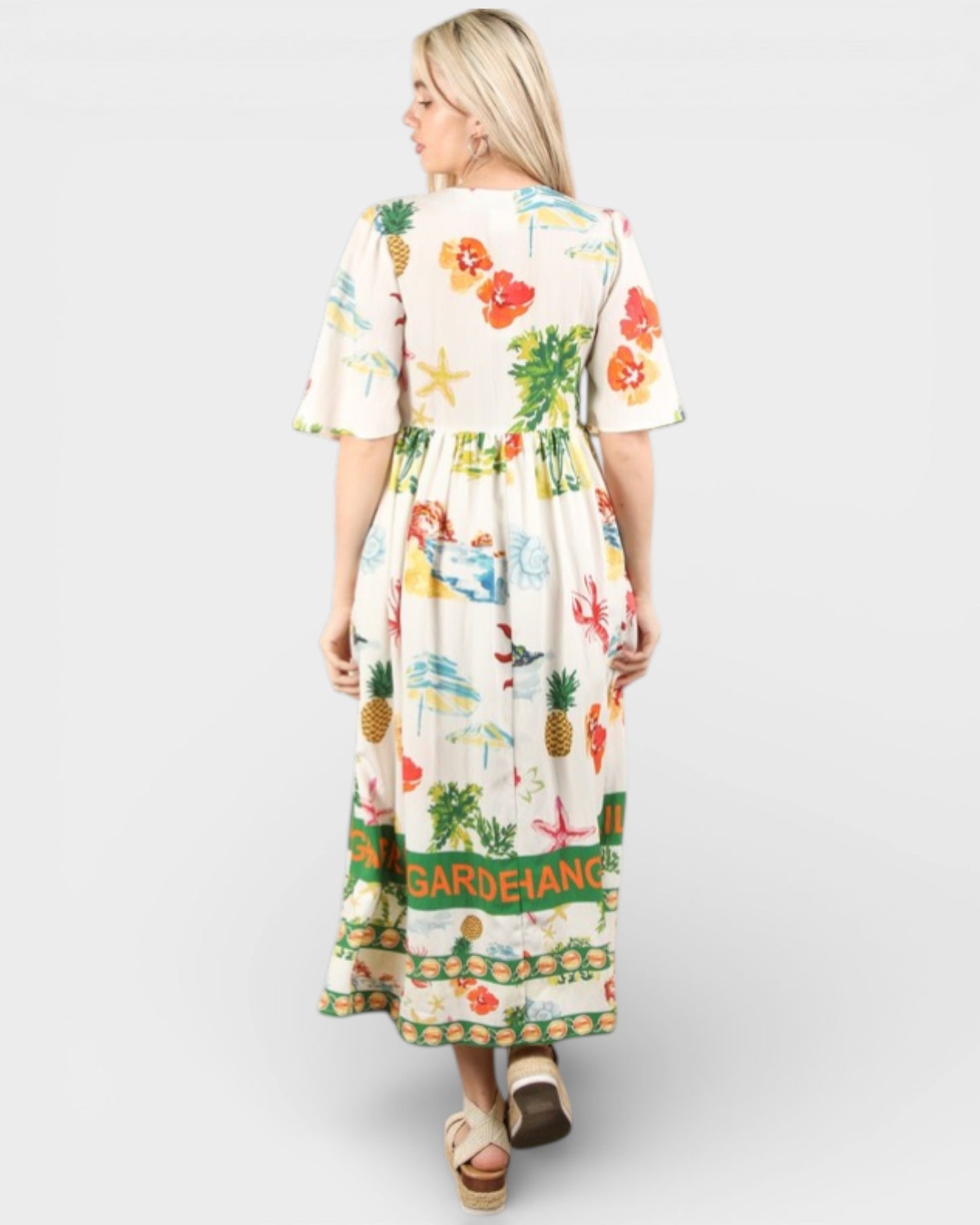 Woman wearing a colorful dress with floral and pineapple patterns on a white background