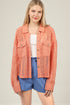 Woman wearing a coral lace jacket over a white top and blue shorts on a beige background