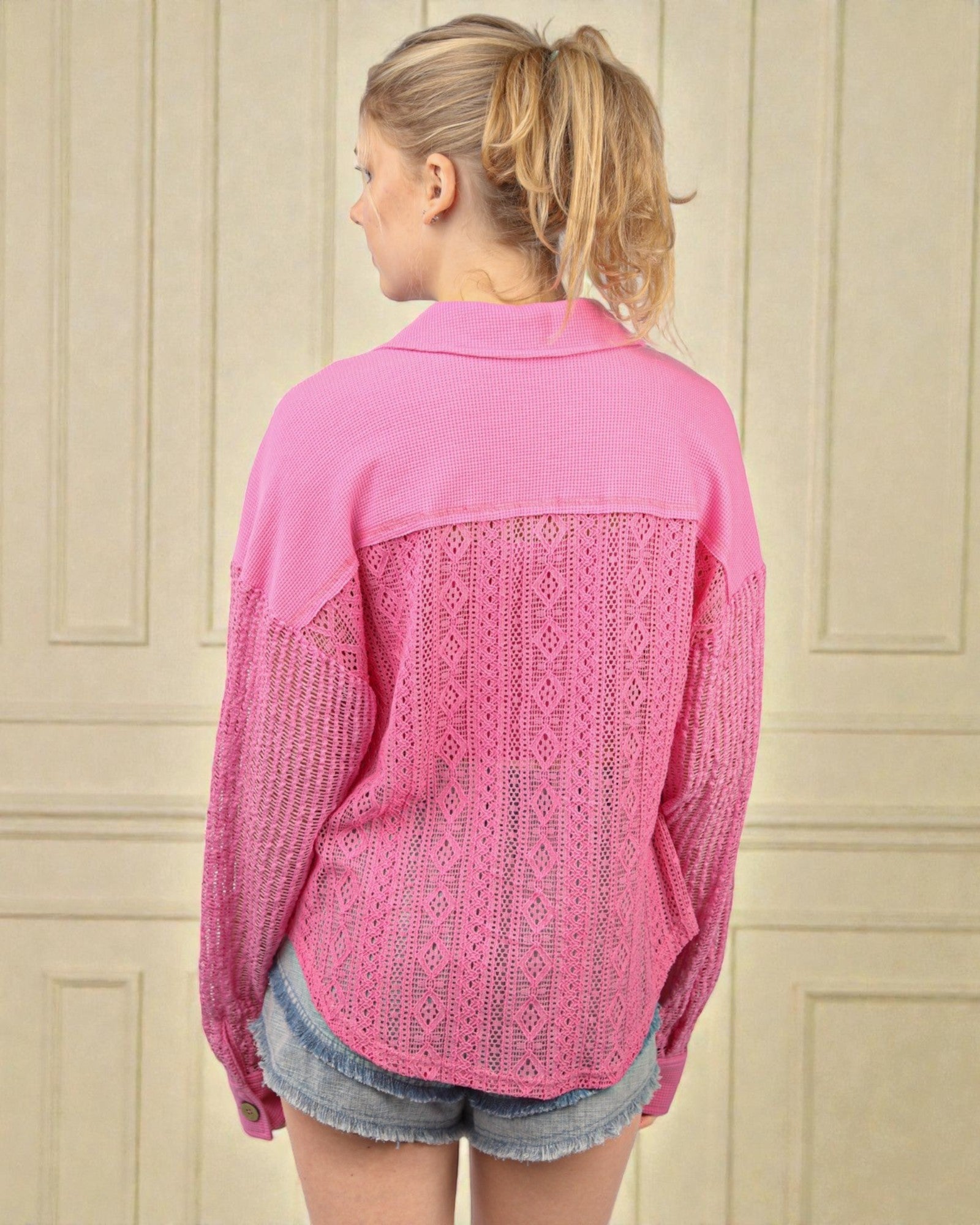 Woman wearing a pink shirt with lace detailing on a beige wall background