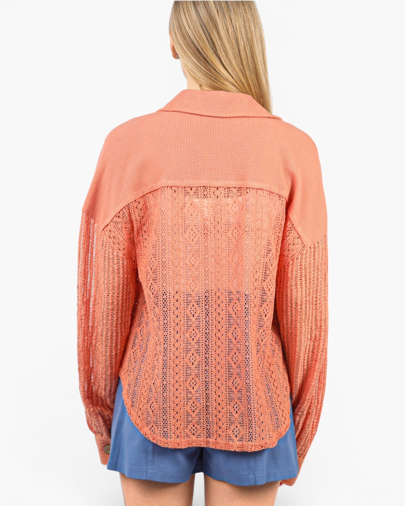 A woman shown from the back wearing a peach-colored open-knit cardigan with textured knit sleeves and collar, paired with blue denim shorts, against a plain white background.
