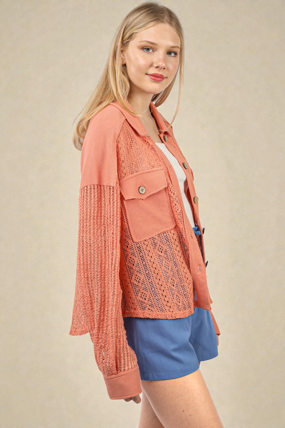Woman wearing a pink crochet jacket and blue shorts on a beige background
