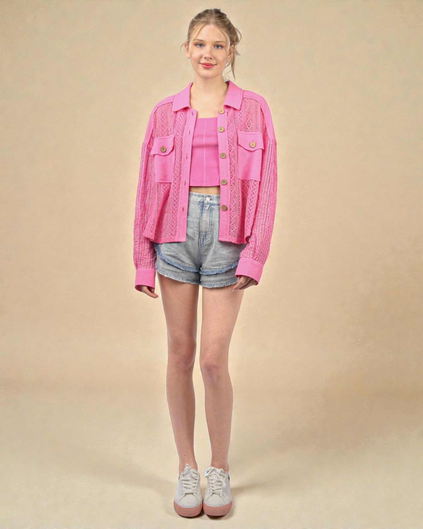 Person wearing a pink jacket, pink top, and denim shorts on a beige background