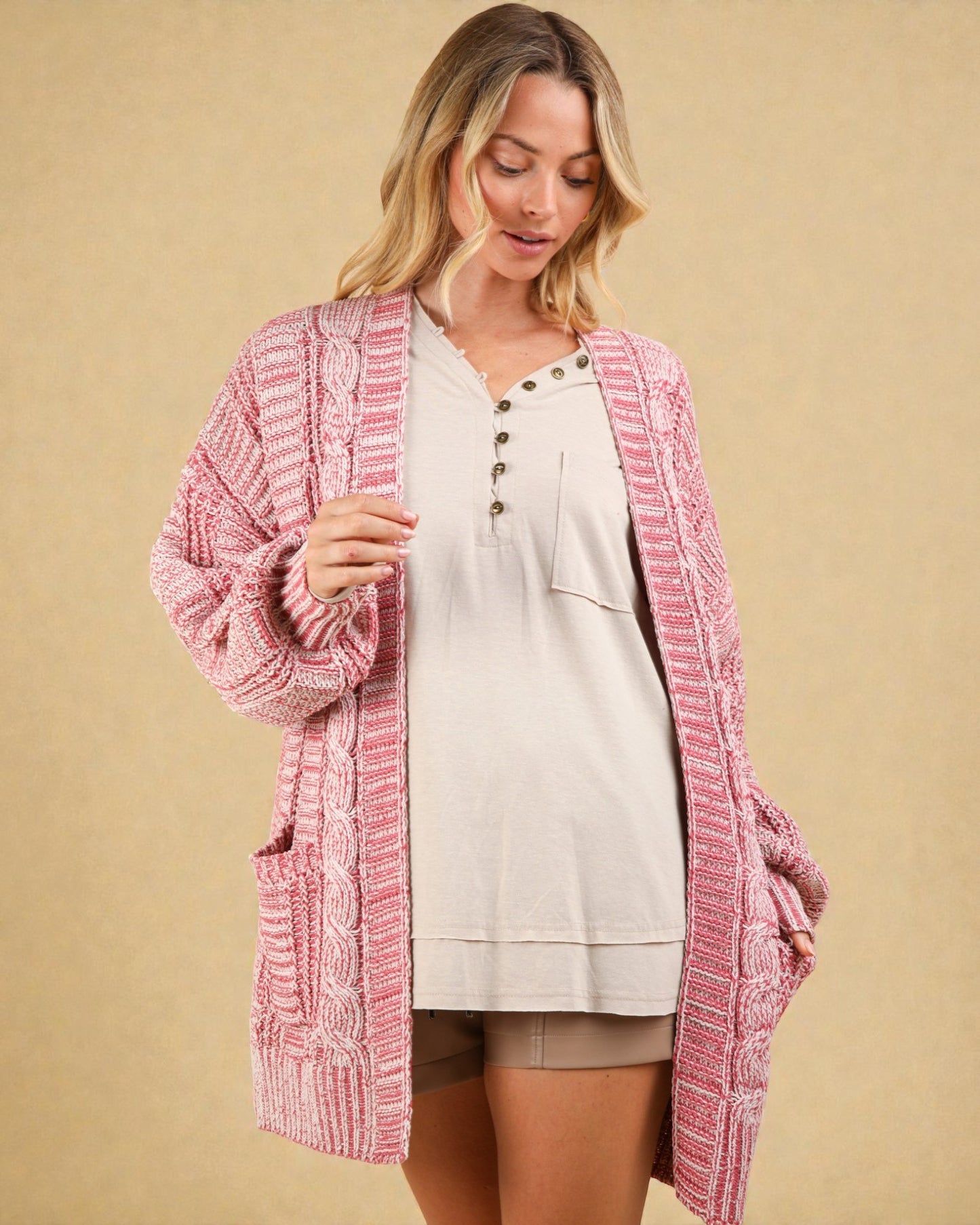 Woman wearing a pink knitted cardigan over a beige top on a beige background