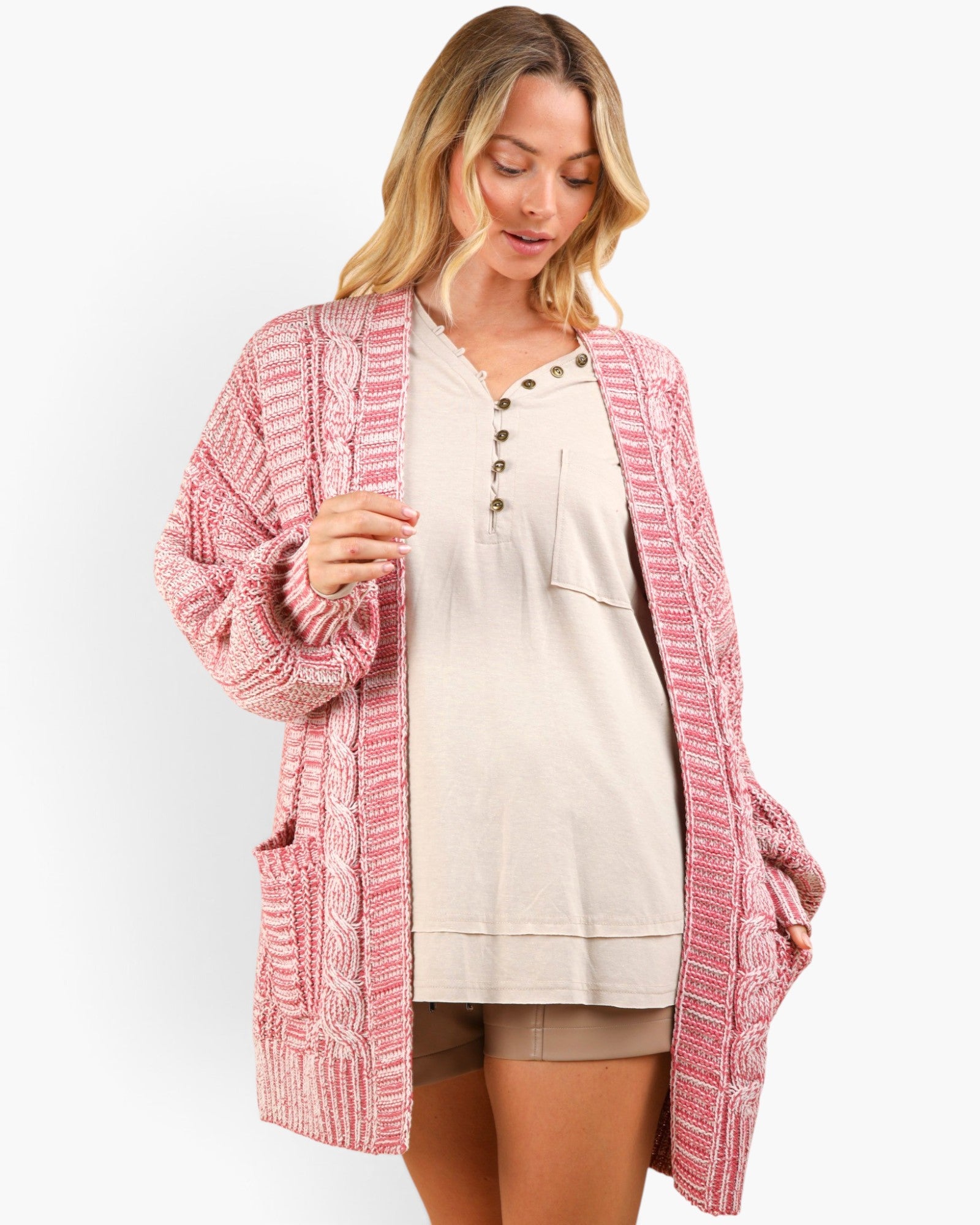 A woman wearing a pink and white textured knit cardigan over a beige henley top and shorts, photographed against a clean white studio background.