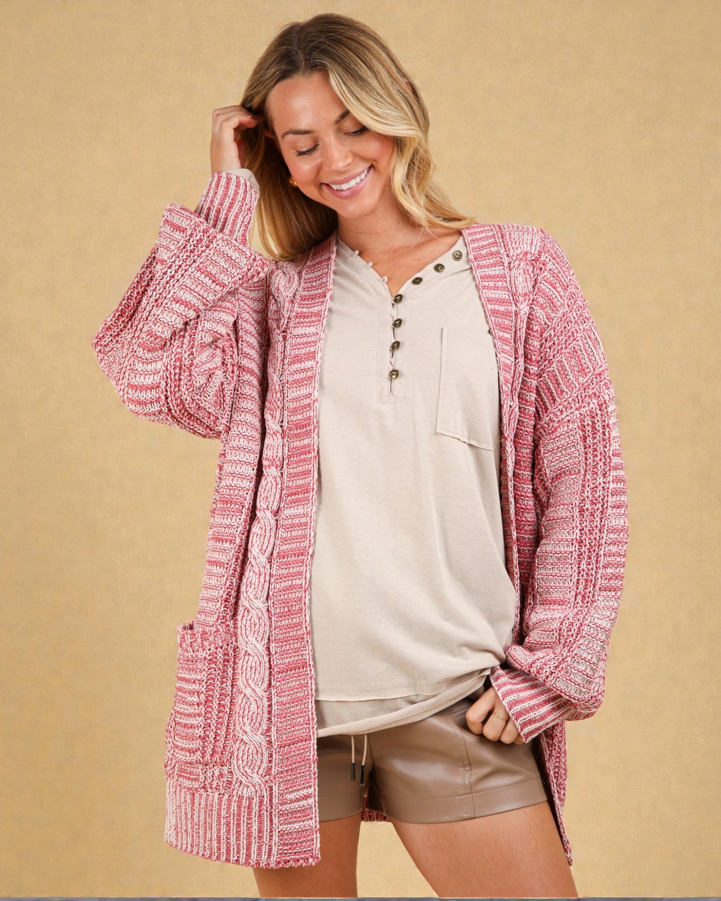 Woman wearing a pink knitted cardigan over a beige shirt and shorts on a beige background
